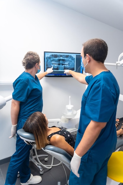 Paciente de clínica odontológica sentada conversando com os dentistas sobre seus dentes olhando para o raio-x