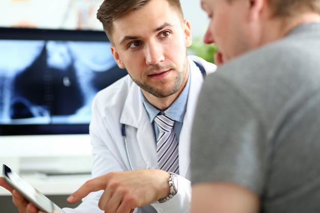 Paciente de consultoria médico masculino bonito mostrando algo no monitor do tablet pc