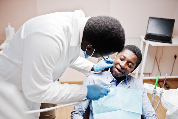 Paciente de homem afro-americano na cadeira odontológica escritório de dentista e conceito de prática médica dentista profissional ajudando seu paciente na odontologia médica perfurando os dentes do paciente na clínica