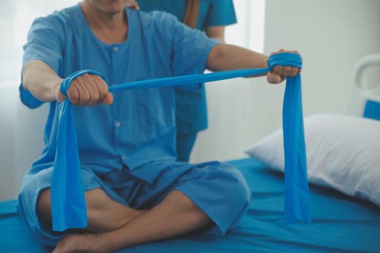 Foto paciente de mão de perto fazendo exercício de alongamento com uma banda de exercício flexível e uma mão de fisioterapeuta para ajudar na sala da clínica
