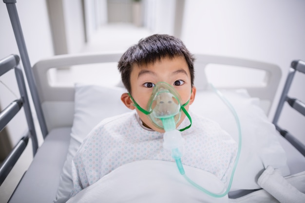 Foto paciente de menino usando máscara de oxigênio, deitado na cama do hospital