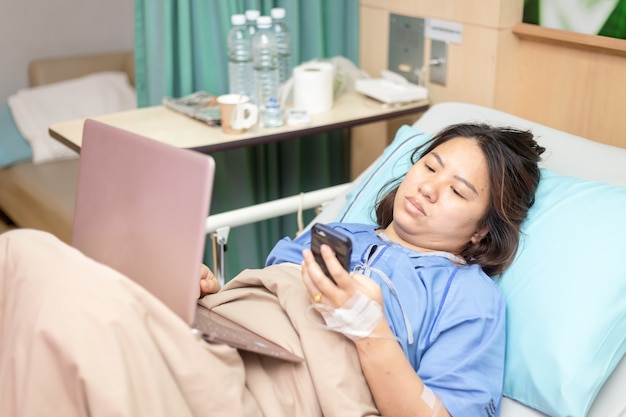 Paciente de mulher asiática trabalhando com laptop durante no hospital