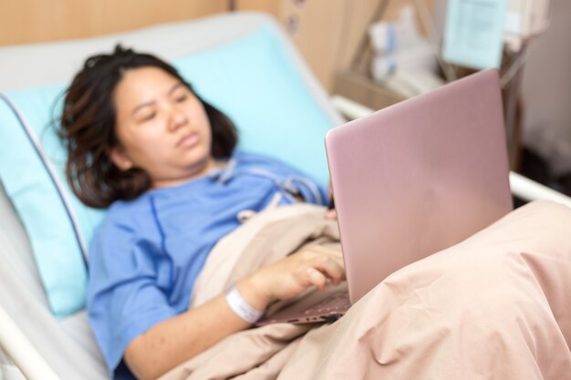 Paciente de mulher asiática trabalhando com laptop durante no hospital