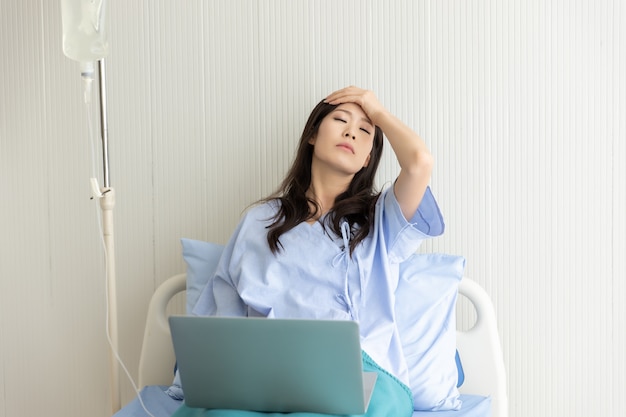 Foto paciente de mulheres asiáticas deitado em uma cama de hospital usando um laptop