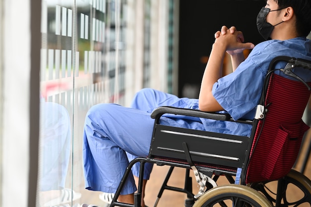 Paciente discapacitado pensativo en silla de ruedas solo en el hospital y mirar por la ventana.