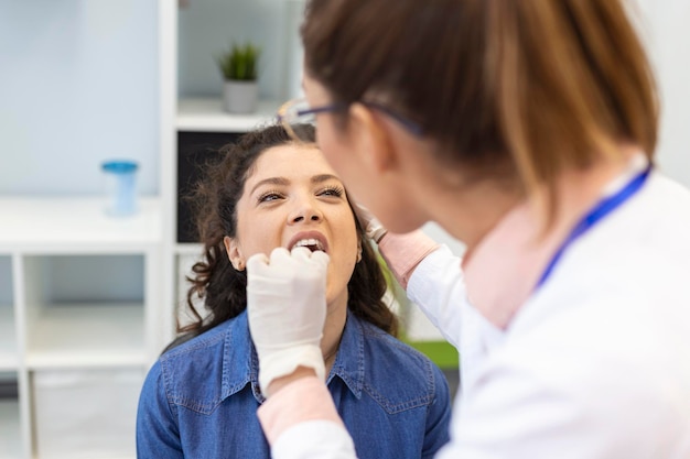 Paciente do sexo feminino abrindo a boca para o médico olhar em sua garganta Otorrinolaringologista examina dor de garganta do paciente