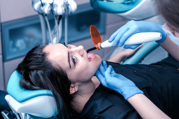 Paciente do sexo feminino com olhos azuis no dentista fazendo obturações dentárias com luz ultravioleta