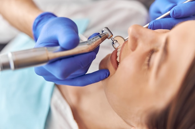 Paciente do sexo feminino em procedimento odontológico, médico usando instrumentos odontológicos na clínica odontológica moderna, close-up.