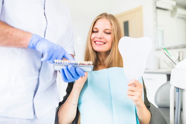 Foto paciente do sexo feminino feliz escolhendo o tom de cor dos dentes dela usando o guia de cores