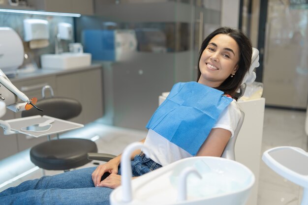 Paciente do sexo feminino feliz muito morena, sentada na cadeira da clínica odontológica.