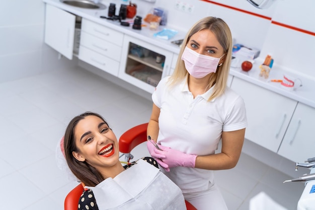 Paciente do sexo feminino feliz olhando para a câmera e desfrutando de um belo sorriso no consultório odontológico Conceito de odontologia e estomatologia Dentista perto do paciente