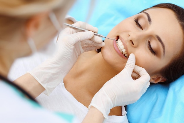 Paciente do sexo feminino jovem visitando o consultório do dentista. Mulher bonita com dentes brancos retos saudáveis, sentado na cadeira odontológica com a boca aberta durante o check-up oral enquanto médico trabalhando nos dentes. Clinica odontológica,