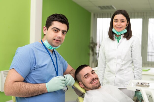 Paciente do sexo masculino com dentista e assistente em um tratamento odontológico usando máscaras e luvas