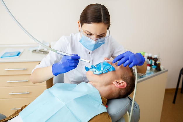 Paciente do sexo masculino se senta na cadeira do dentista e recebe restauração dos dentes, dentista do sexo feminino na clínica odontológica. Foco seletivo