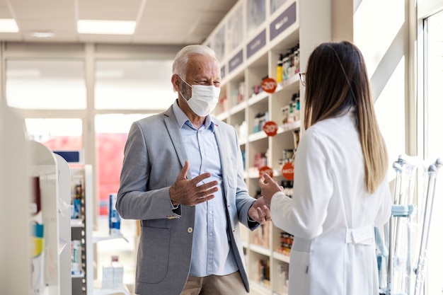 Un paciente en una farmacia. Un anciano habla con una farmacéutica y le explica algo con las manos.