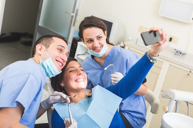 Paciente feliz, dentista y asistente tomando autofoto todos juntos.