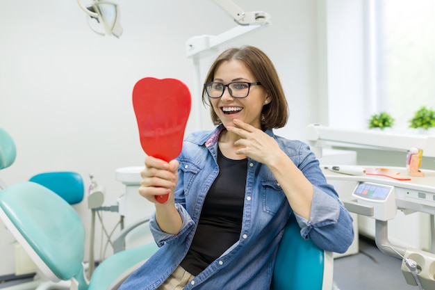 Paciente feliz mulher olhando no espelho para os dentes