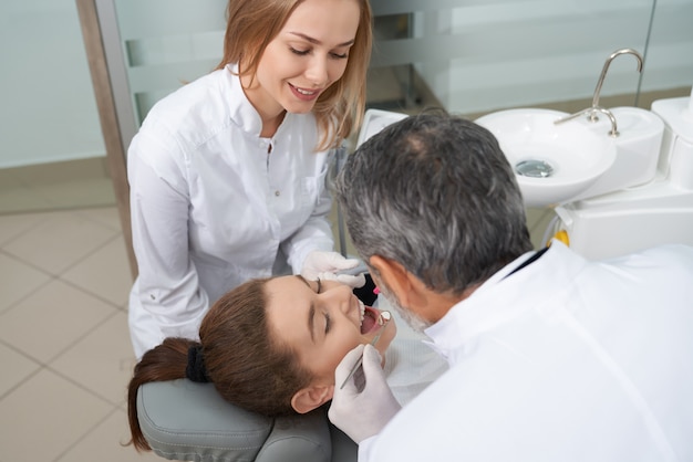 Paciente femenino con la boca abierta y el dentista revisando los dientes