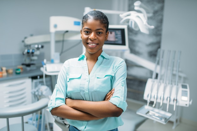 Paciente femenino sonriente en la clínica dental, equipo médico en el fondo. Mujer en gabinete de odontología, estomatología, cuidado de los dientes