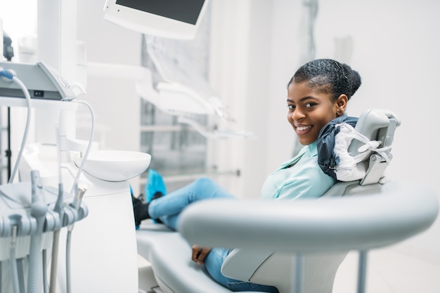 Paciente femenino sonriente en silla, visita en clínica dental.