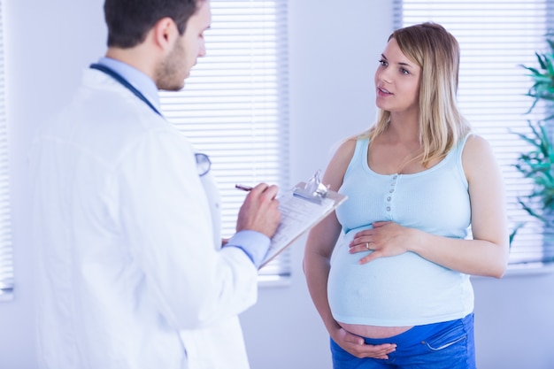 Paciente grávida falando com o médico que está tomando notas