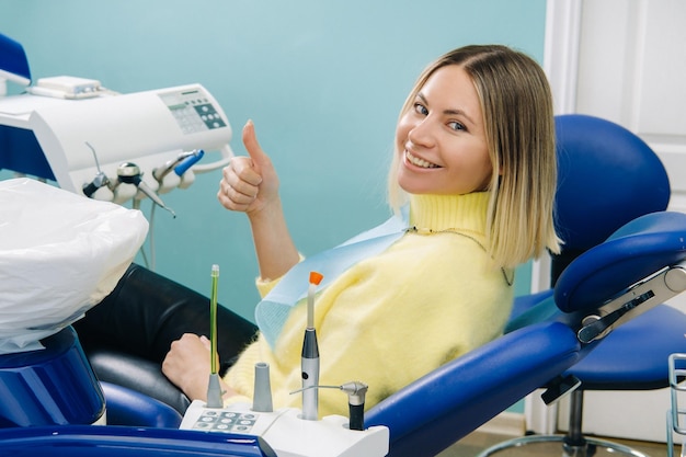 Paciente hermosa chica muestra la clase con la mano mientras está sentado en la silla del dentista.