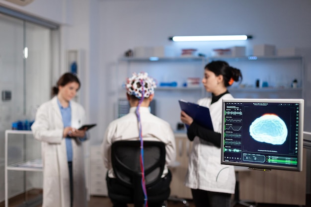 Paciente hombre con auriculares eeg para exploración cerebral de pie en laboratorio neurológico durante el experimento de neurología. Equipo médico de científicos que monitorean la actividad cerebral analizando el sistema nervioso