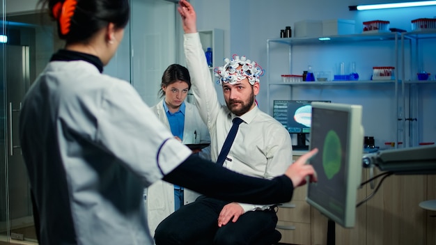 Paciente hombre con dispositivo de auriculares de alta tecnología que participa en un experimento neurológico en un laboratorio tecnológicamente avanzado que prueba las reacciones físicas y el sistema nervioso