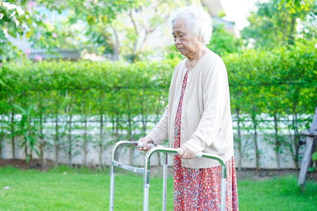 Paciente idosa asiática com deficiência anda com caminhante no conceito médico do parque