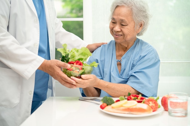 Paciente idosa asiática comendo bife de salmão no café da manhã com comida vegetal saudável no hospital