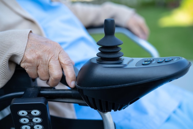 Paciente idosa asiática em cadeira de rodas elétrica com joystick e controle remoto no hospital