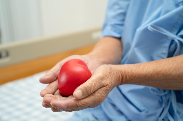 Paciente idosa asiática segurando coração vermelho na mão na cama no hospital conceito médico forte e saudável