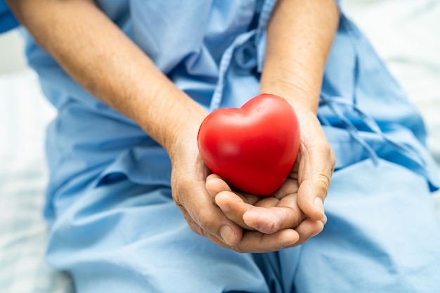 Paciente idosa asiática segurando coração vermelho na mão na cama no hospital