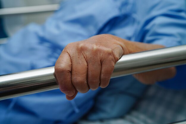 Paciente idosa asiática segurando o trilho da cama enquanto se deita com esperança esperando sua família no hospital