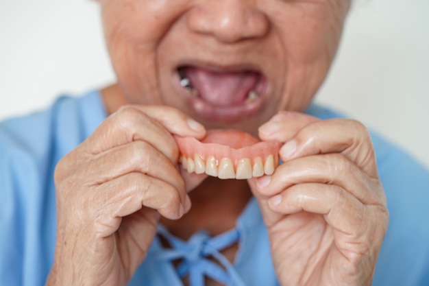 Paciente idosa asiática usando dentadura de dentes na boca para mastigar comida
