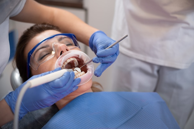 Paciente jovem com óculos de proteção e afastador de boca durante o tratamento no consultório dentista.