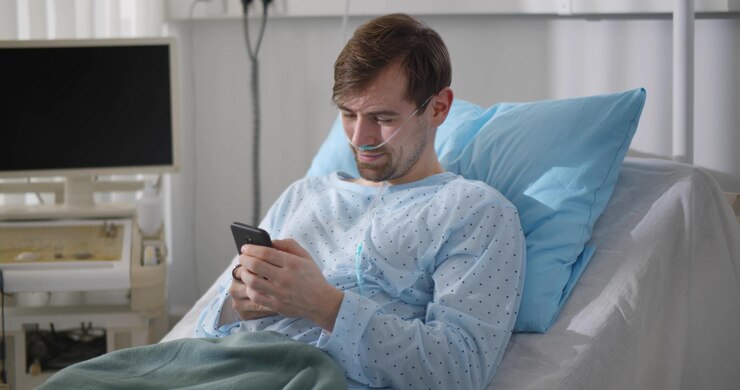 Paciente joven acostado en la cama del hospital y usando un teléfono inteligente mientras se recupera en el hospital