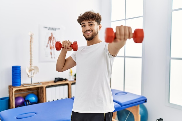 Paciente joven árabe haciendo rehabilitación usando pesas en la clínica