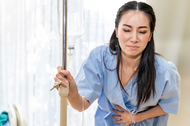 Paciente joven asiática caminando y dolor menstrual en la habitación del hospital.