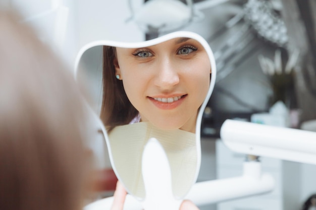 Una paciente joven mira sus dientes en el espejo Clínica dental moderna blanqueamiento de dientes