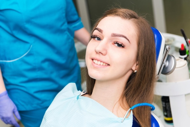 Paciente joven sonríe en una silla al médico en el consultorio dental