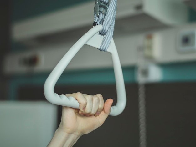 Paciente masculino caucasiano segurando com uma mão um arco terapêutico triangular com uma pinça colocada acima da cama em uma sala de hospital vista lateral de close-up O conceito de dispositivos de trauma
