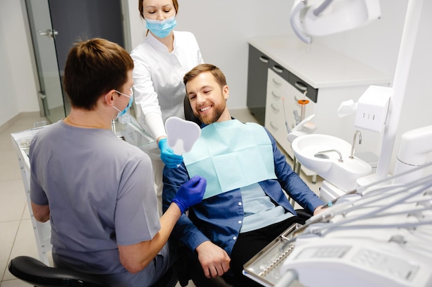 Paciente masculino guapo mirando su hermosa sonrisa sentado en el consultorio dental