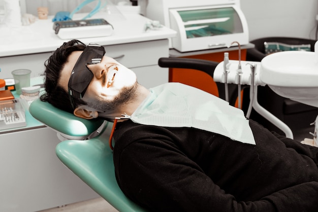 Un paciente masculino joven y satisfecho en la silla del dentista. Sonriendo a la cámara. Salud y Medicina.