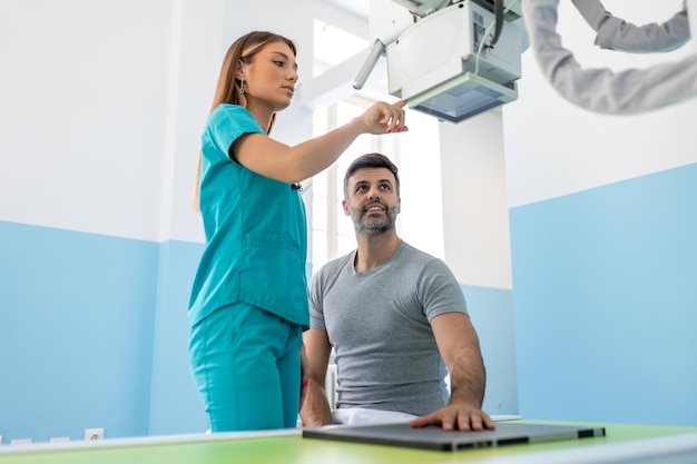 Foto paciente masculino sentado mientras una enfermera ajusta una máquina de rayos x moderna para escanear su brazo o mano en busca de lesiones y fracturas