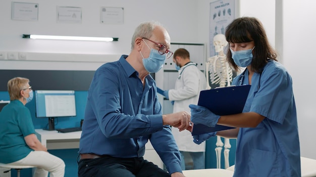 Paciente mayor que firma documentos de control para recibir tratamiento después de asistir a la consulta médica con la enfermera en el consultorio. Anciano firmando archivos en la visita de examen con un especialista.