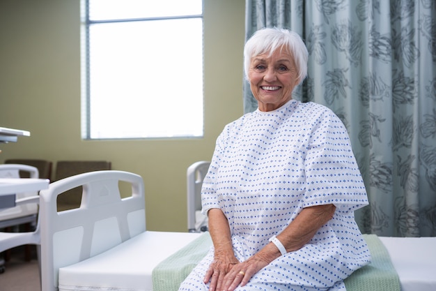 Paciente mayor sonriente sentado en la cama en el hospital