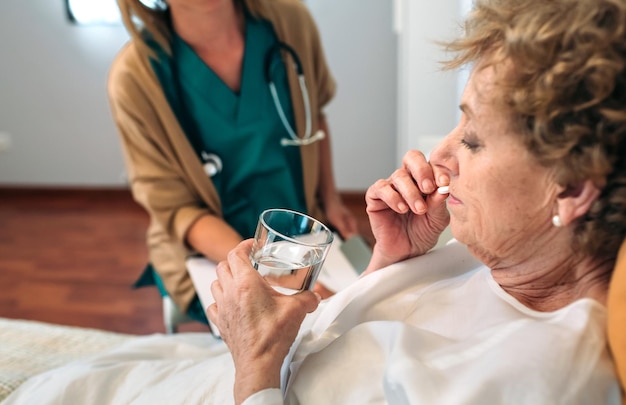 Paciente mayor tomando una pastilla junto a su doctora