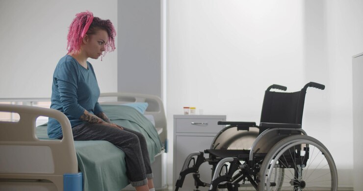 Paciente mujer joven sentada en la cama del hospital mirando la silla de ruedas