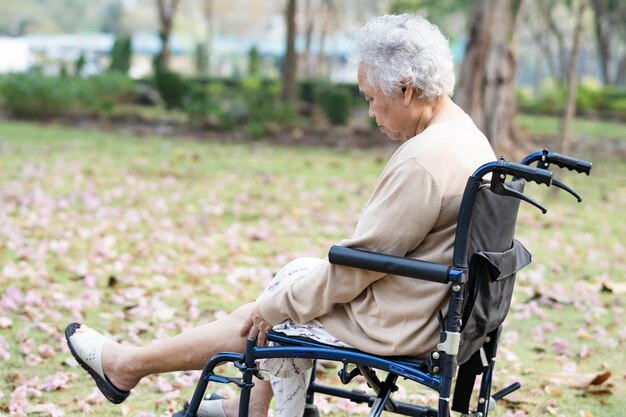 Paciente mujer mayor asiática dolor de rodilla en silla de ruedas en el parque.